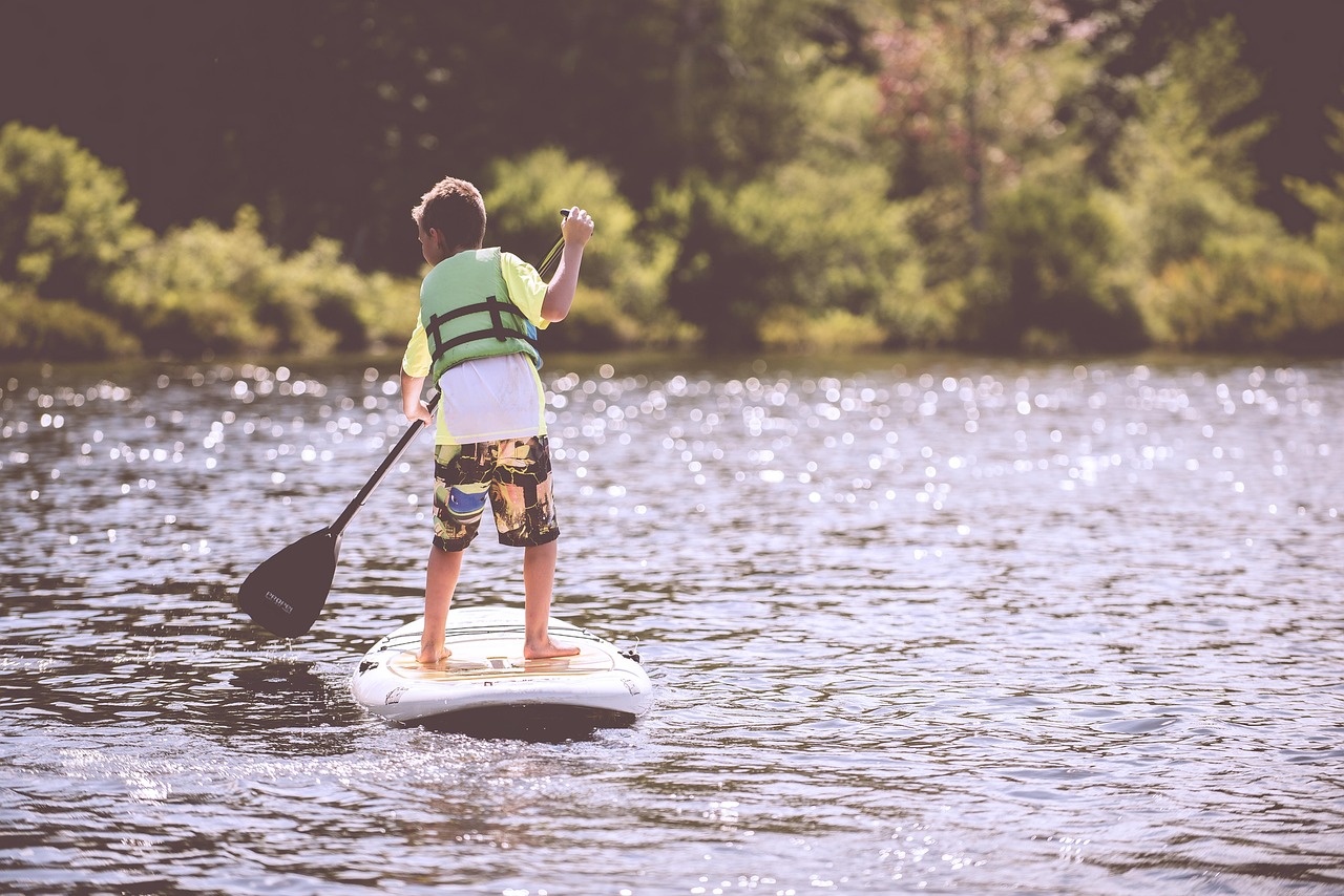 boy, paddleboard, paddle, life jacket, pond, lake, paddleboarding, paddleboarder, child, fun, kid, leisure, life vest, outdoors, nature, person, recreation, river, surfboard, water, water sports