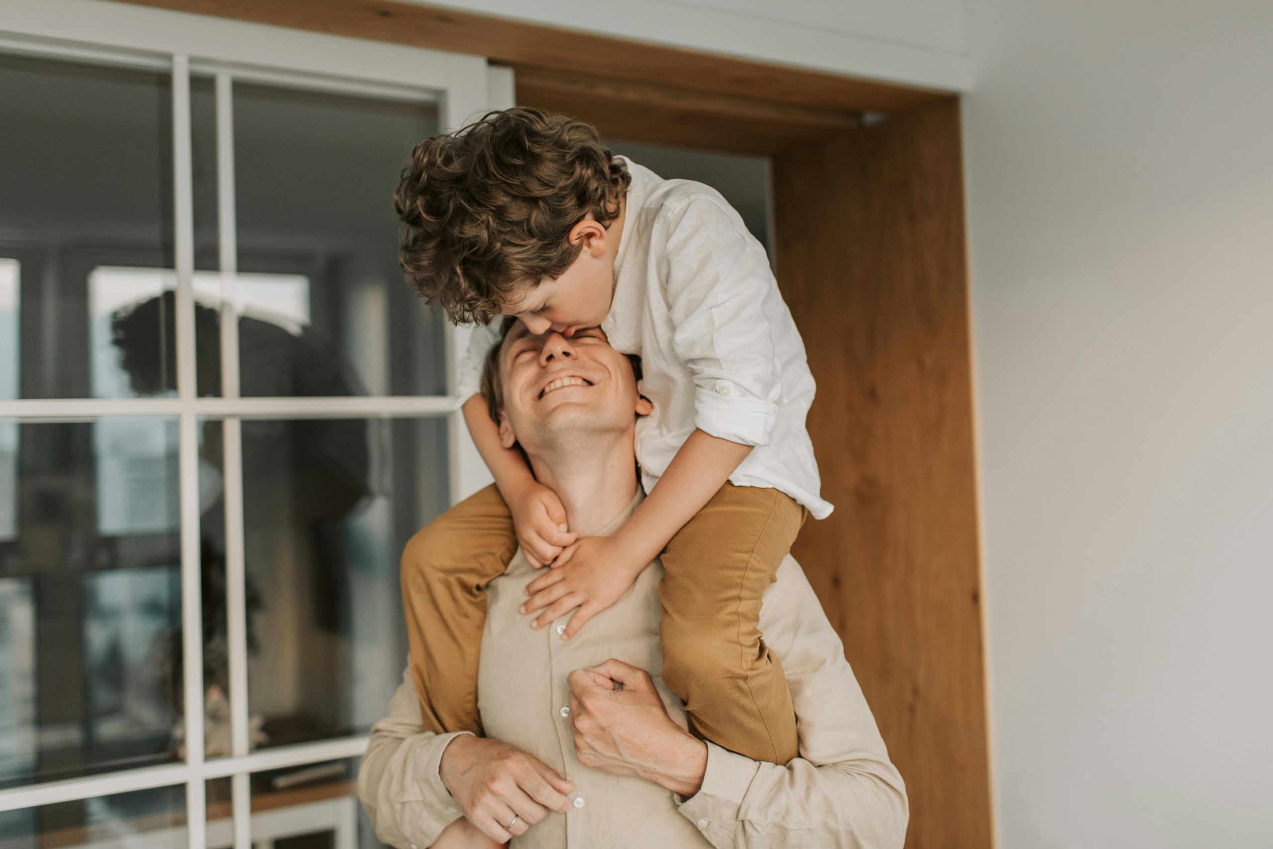 A joyful moment of a father carrying his son on his shoulders indoors.