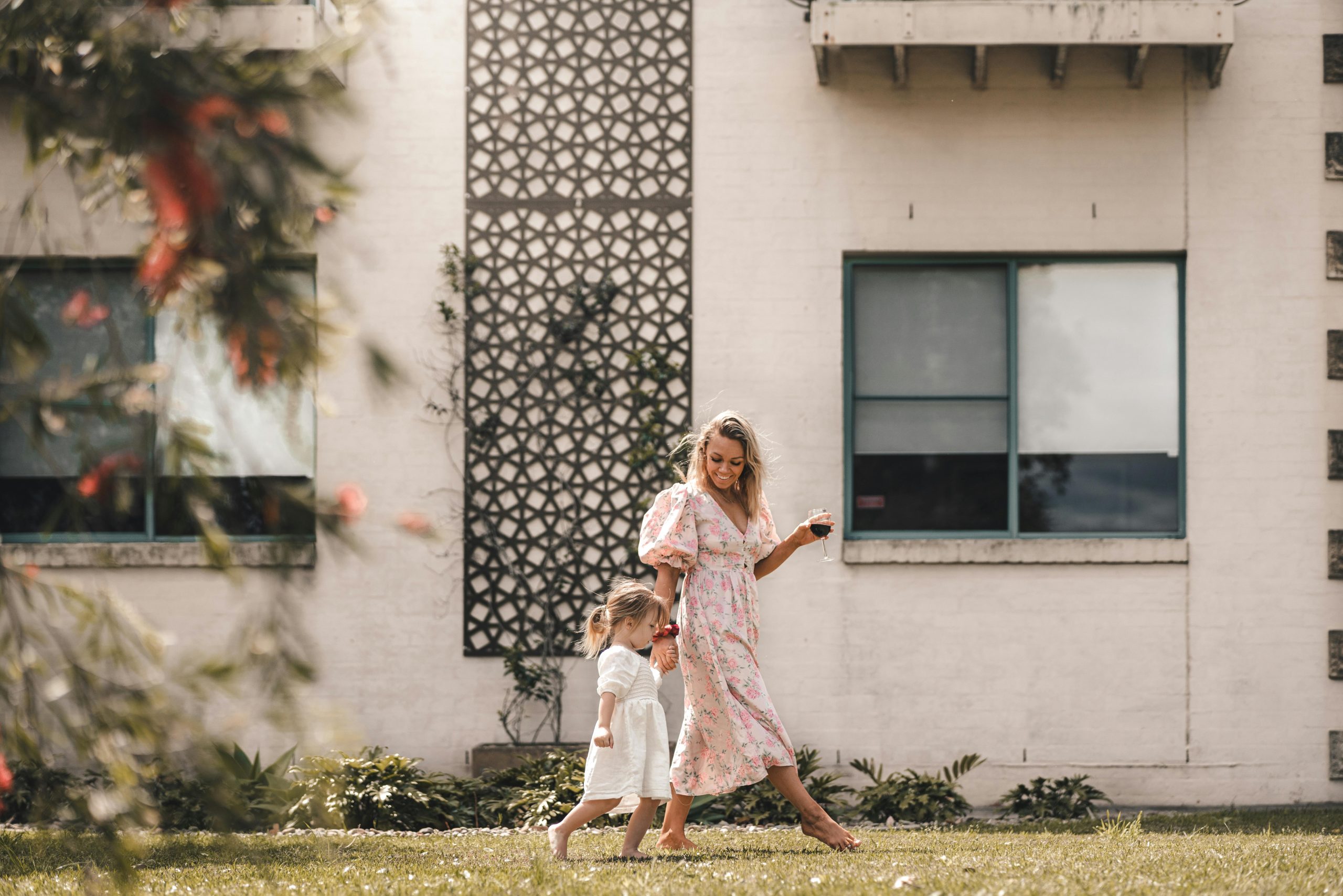 A joyful mother and daughter walking hand in hand in a sunny backyard setting.