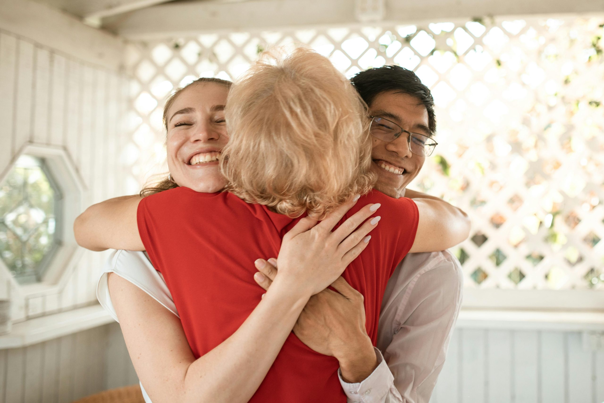 Three adults share a warm embrace, radiating happiness in a cozy indoor environment.