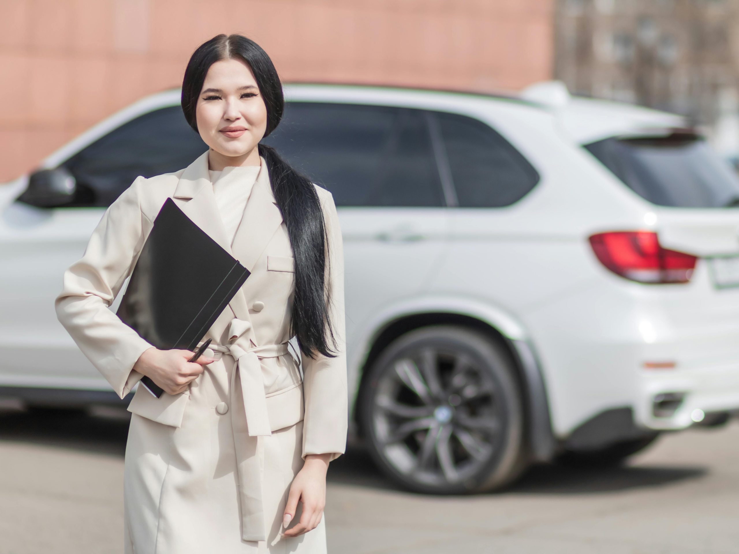 Smiling professional woman standing confidently by a luxury car, embodying success.
